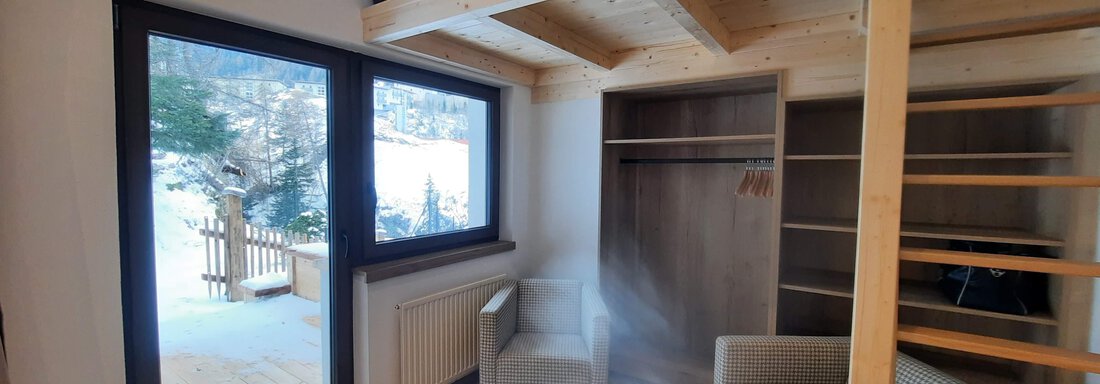 A modern room with wood veneer and a sleeping area on a mezzanine. Through the large window front, you can see a snowy landscape. - Ferienhaus Anna - Sölden