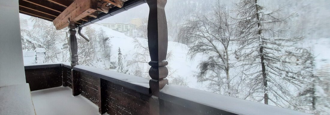 A balcony with wooden cladding, surrounded by snow-covered trees and a wintry landscape. The snow forms a white blanket on the ground. - Ferienhaus Anna - Sölden