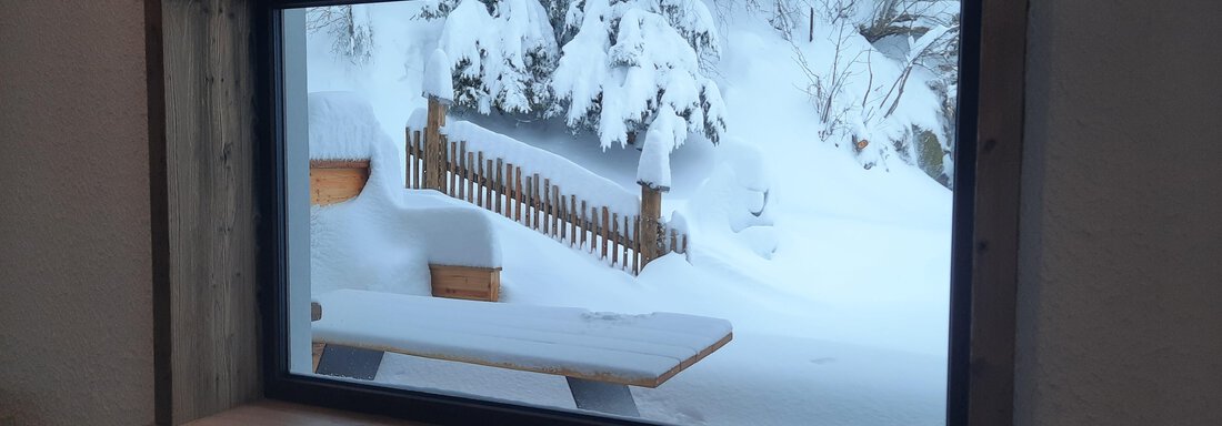 A window view of a snowy landscape. Snow covers the trees and the garden furniture outside. - Ferienhaus Anna - Sölden