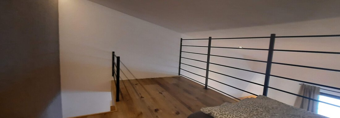 A cozy bedroom in the attic with two beds and wooden floor. The walls are simple and there is a metal railing. - Ferienhaus Anna - Sölden