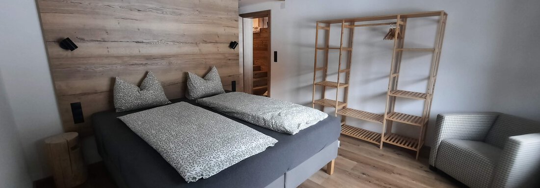A modern bedroom with two beds and wood paneling. There is a cozy armchair and a wooden bookshelf. - Ferienhaus Anna - Sölden