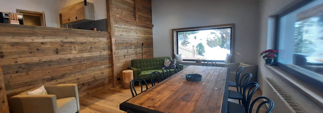 A modern room with wooden paneling and large windows. A long dining table is the centerpiece of the living room, surrounded by stylish chairs. - Ferienhaus Anna - Sölden