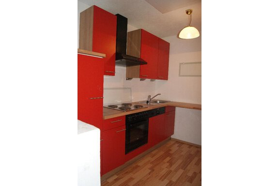 A modern kitchen with red cabinets and wooden surfaces. It features a stove, a sink, and a range hood. - Ferienhaus Anna - Sölden