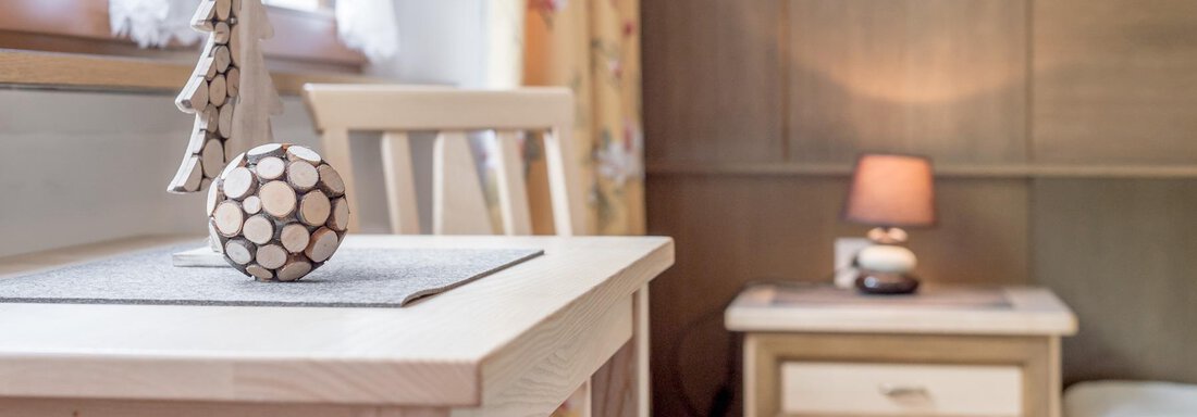 A cozy room with a wooden table and a chair. On the table is a decorative wooden figure and a table lamp emits warm light. - Ferienhaus Apart Sonnzeit - Sölden