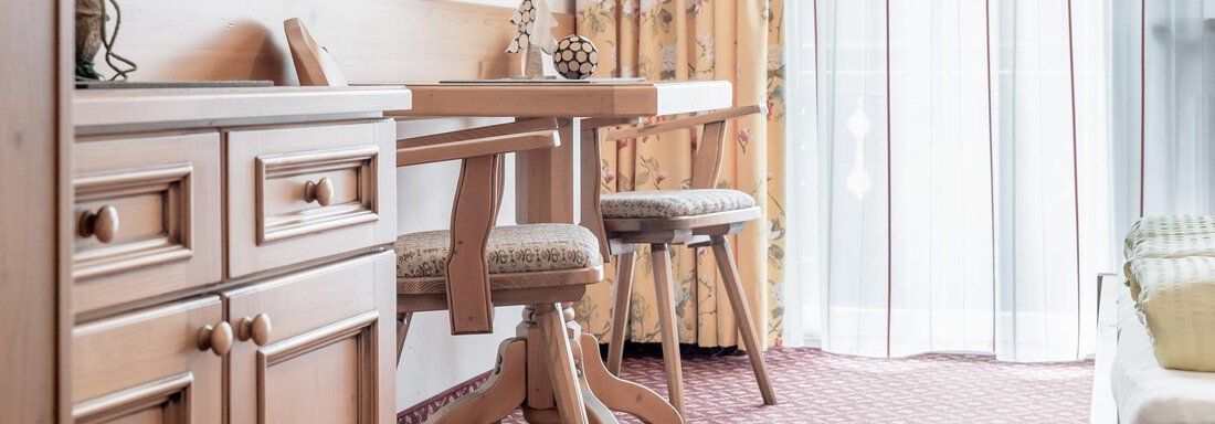 A cozy room with wooden furniture and two stools. Large windows provide plenty of daylight and an inviting atmosphere. - Ferienhaus Apart Sonnzeit - Sölden
