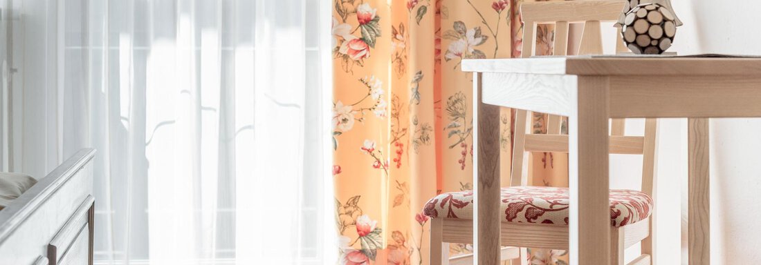 A bright room with a table and two chairs. Curtain with floral patterns and a small Christmas tree decoration. - Ferienhaus Apart Sonnzeit - Sölden