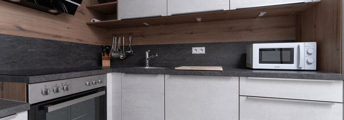 A modern kitchen with wood and gray elements. It is equipped with a stove, a microwave, and a sink. - Ferienhaus F2 - Sölden - Sölden