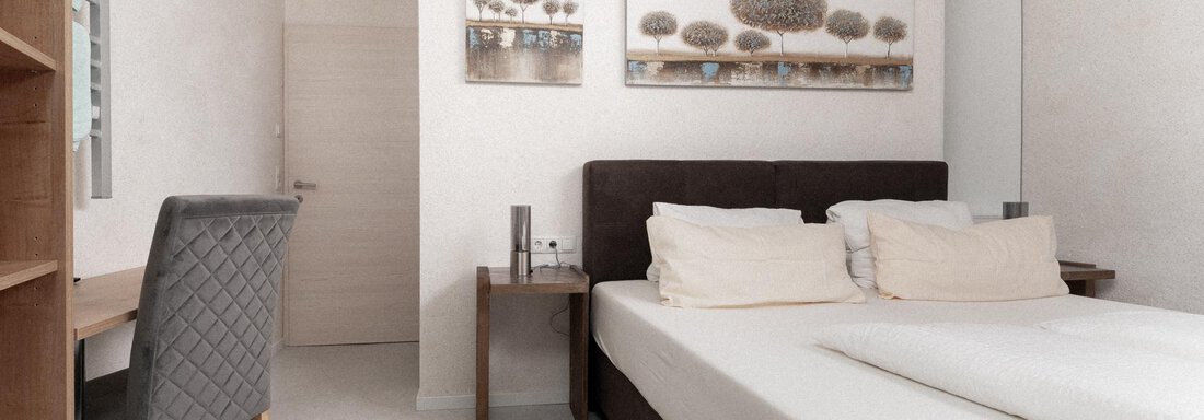 A modern bedroom with a large double bed and two nightstands. The room is bright and simply furnished, with a desk and a sofa. - Ferienhaus F2 - Sölden - Sölden