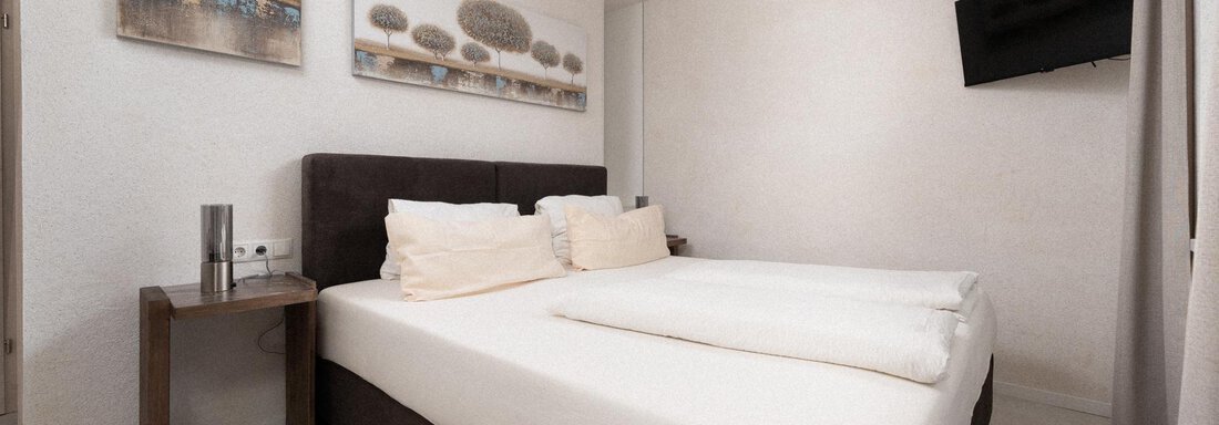 A bright bedroom with a large double bed and two pillows. Pictures hang on the wall and a television is also visible. - Ferienhaus F2 - Sölden - Sölden