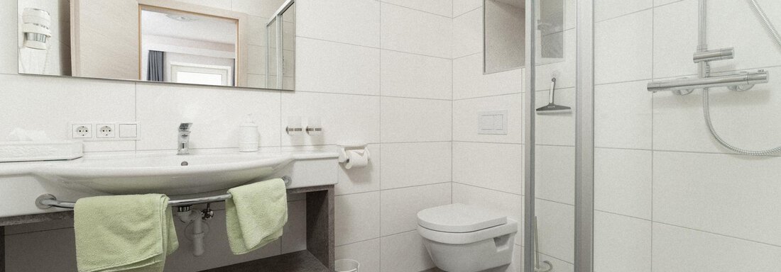 A modern bathroom with a shower, sink, and toilet. The walls are bright tiled and there are towels in fresh green. - Ferienhaus F2 - Sölden - Sölden