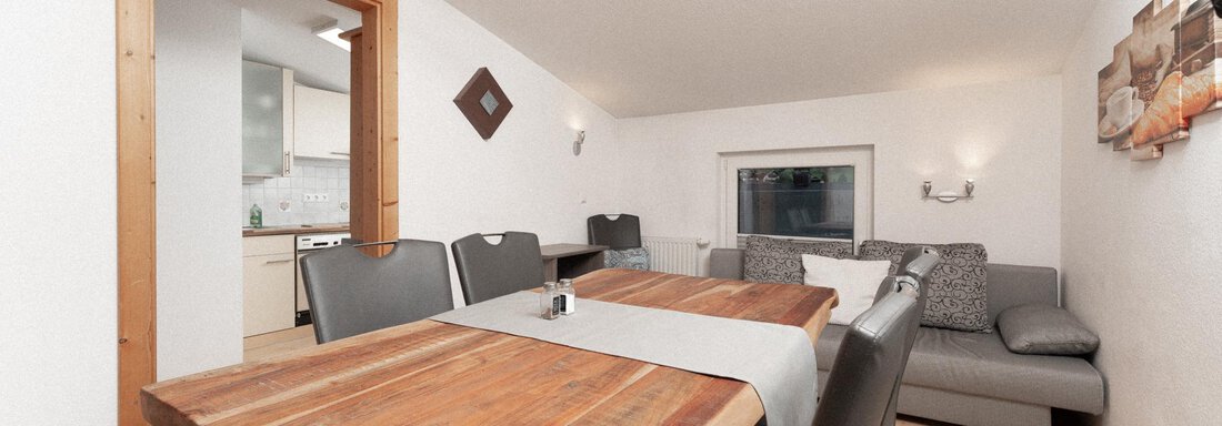 A cozy dining area with a large wooden table and modern chairs. In the background, a seating area and an open kitchenette are visible. - Ferienhaus F2 - Sölden - Sölden