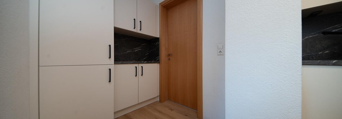 A modern kitchen with white cabinets and a dark workspace. The wooden beams and the wooden floor give the room a warm atmosphere. - Ferienhaus F2 - Sölden - Sölden