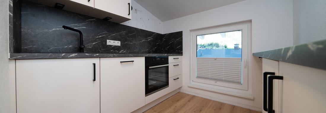 A modern kitchen with white cabinets and an elegant black countertop. The room has a window that lets in natural light. - Ferienhaus F2 - Sölden - Sölden