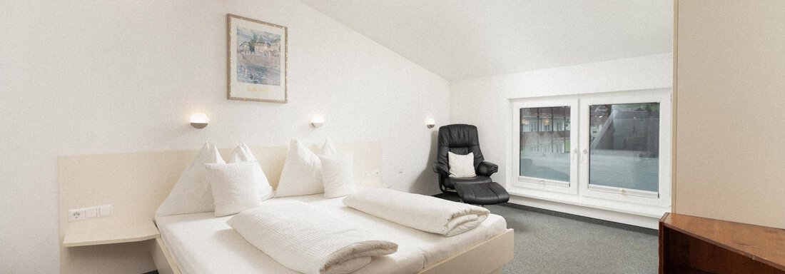 A modern bedroom with a double bed and fresh white bedding.  
Large windows let in plenty of light and offer a view of the surroundings. - Ferienhaus F2 - Sölden - Sölden