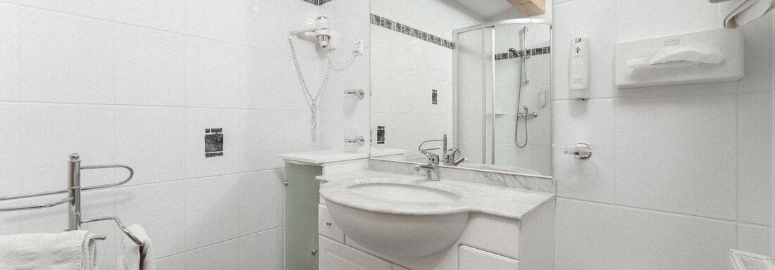 A modern bathroom with white tiles and a large mirror surface. The amenities include a sink, a shower, and towels. - Ferienhaus F2 - Sölden - Sölden