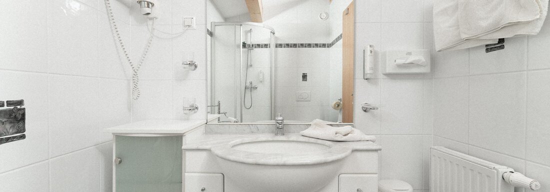 A modern bathroom with white tiles and a large mirror. There is a shower, a sink, and a towel holder. - Ferienhaus F2 - Sölden - Sölden