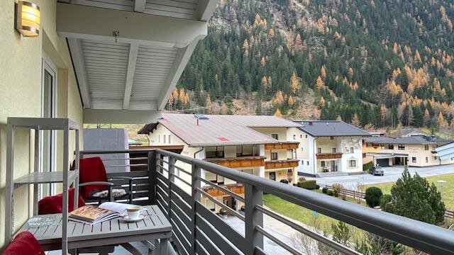 A cozy balcony with red chairs and a table. In the background, the mountains and some houses can be seen. - Ferienhaus F2 - Sölden - Sölden
