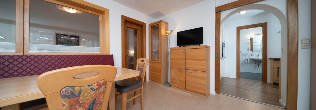 A cozy dining area with a wooden table and colorful chairs. In the background, additional rooms and a television are visible. - Ferienhaus F2 - Sölden - Sölden