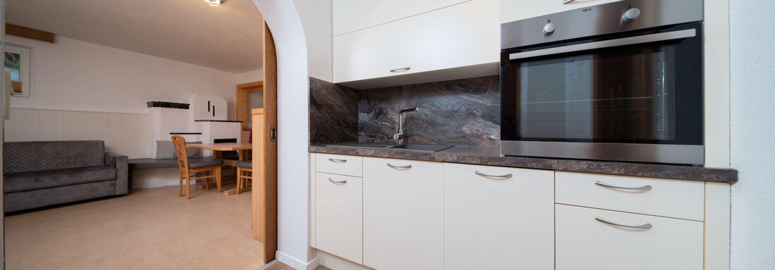 A modern kitchen with white cabinets and an elegant oven. In the background, there is a dining area with a table and chairs. - Ferienhaus F2 - Sölden - Sölden