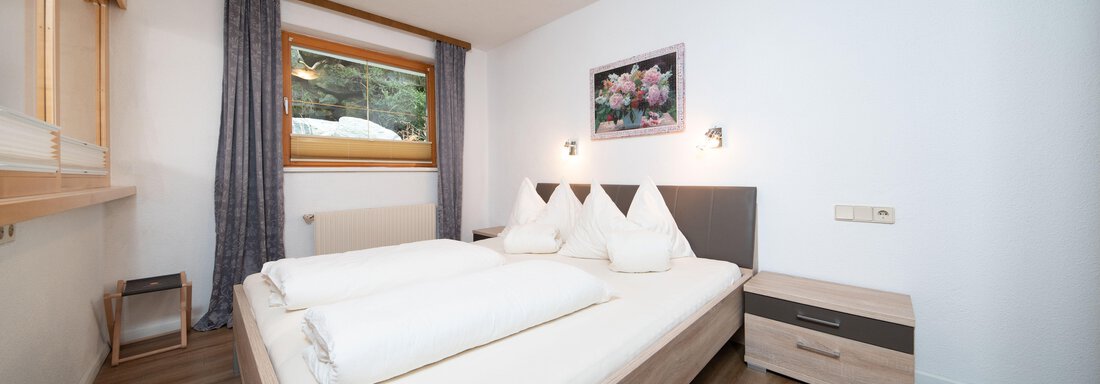 A cozy bedroom with a large bed and bright bedding. There is a window with a view and a modern bedside lamp. - Ferienhaus F2 - Sölden - Sölden
