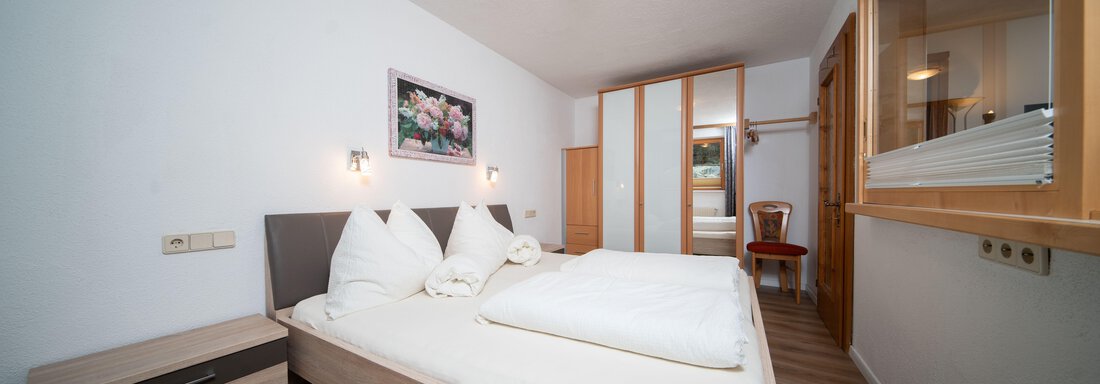 A cozy bedroom with two beds and modern furniture. The walls are bright, and a beautiful floral wallpaper is visible. - Ferienhaus F2 - Sölden - Sölden