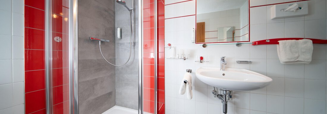 A modern bathroom with a shower and a sink. The walls are tiled in white and red, and the floor is made of dark stone. - Ferienhaus F2 - Sölden - Sölden