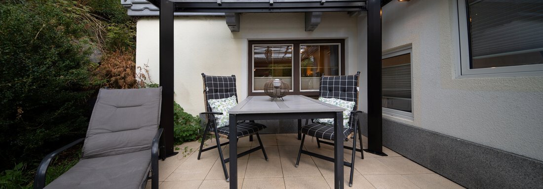 A cozy terrace with a table and chairs under a transparent roof. There is also a lounge chair and a green environment. - Ferienhaus F2 - Sölden - Sölden