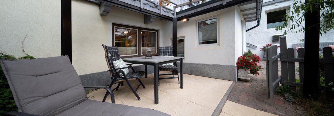 A cozy outdoor area with a table and chairs under a canopy. A lounge chair invites you to relax, surrounded by beautiful plants. - Ferienhaus F2 - Sölden - Sölden