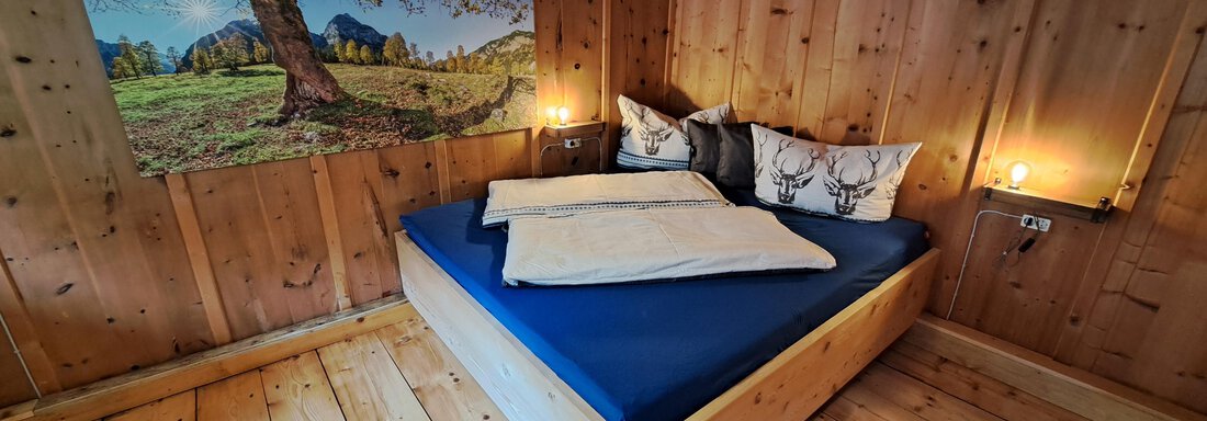 A cozy wooden bedroom with a large bed and decorative pillows. A picture of a picturesque landscape hangs on the wall. - Ferienhaus Kaspers - Sölden