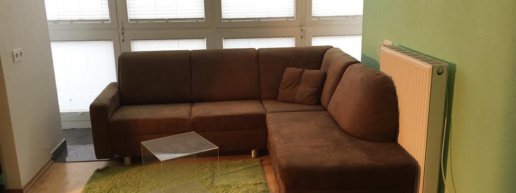 A cozy living room with a brown sofa and a green carpet. Large windows provide plenty of daylight. - Ferienhaus Moidl - Sölden