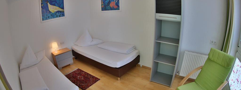 A simple room with two beds and a cozy armchair. The walls are decorated with colorful pictures, and the floor is made of wood. - Ferienhaus Moidl - Sölden