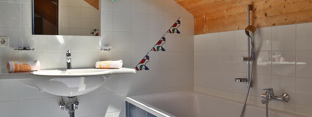 A modern bathroom with a bathtub and a sink. The walls are tiled white and the ceiling is made of wood. - Ferienhaus Moidl - Sölden