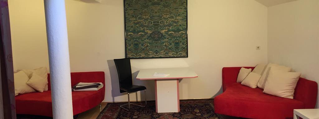 A modern room with red sofas and a white table. The floor is covered with a colorful carpet and a decorative picture hangs on the wall. - Ferienhaus Moidl - Sölden