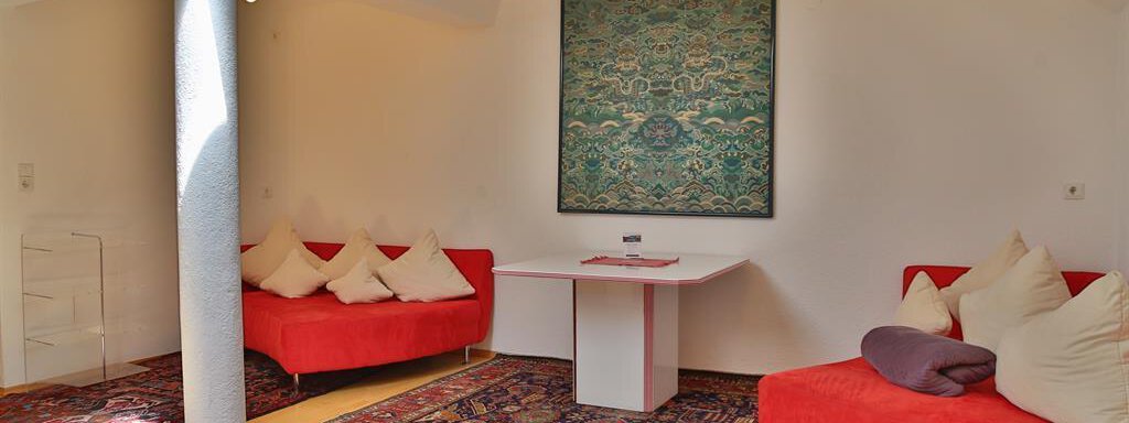 A modern living room with red sofas and a colorful rug. A decorative artwork hangs on the wall. - Ferienhaus Moidl - Sölden