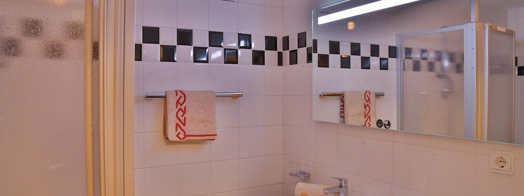 A modern bathroom with a shower, a large mirror, and a sink. It is designed in light colors with some black accents. - Ferienhaus Moidl - Sölden