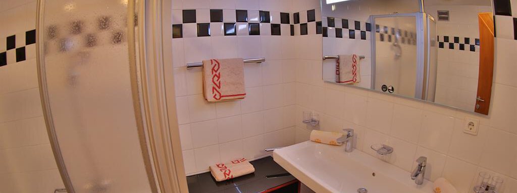 A modern bathroom with a shower and bathtub. The walls are designed in white with black tile accents. - Ferienhaus Moidl - Sölden