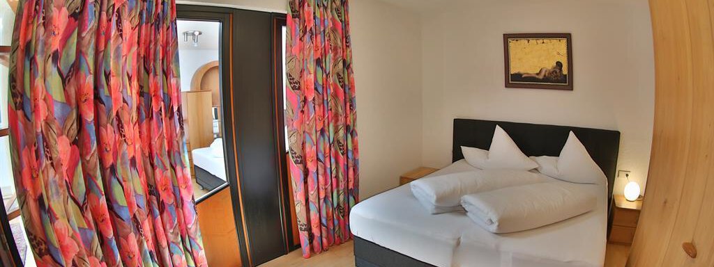 A cozy bedroom with a double bed and colorful curtains. The room has plenty of daylight and a warm atmosphere. - Ferienhaus Moidl - Sölden