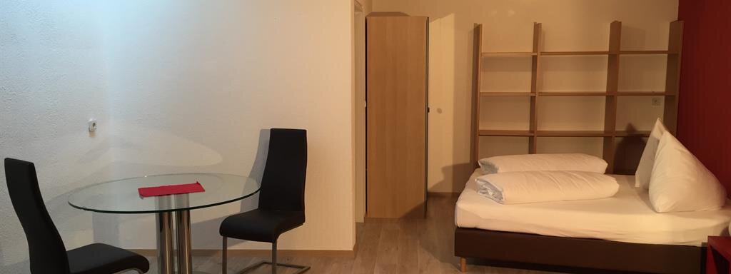 A simple, modern room with a bed and a small dining table. There are chairs, a red carpet, and a bright environment. - Ferienhaus Moidl - Sölden