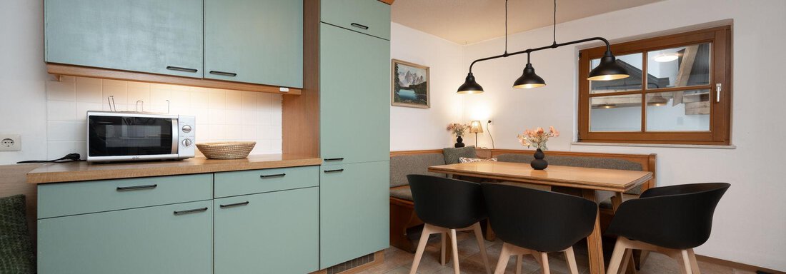 A modern kitchen with mint green cabinets and a dining area. The room has warm lighting and wooden details. - Ferienhaus Valsora - Sölden
