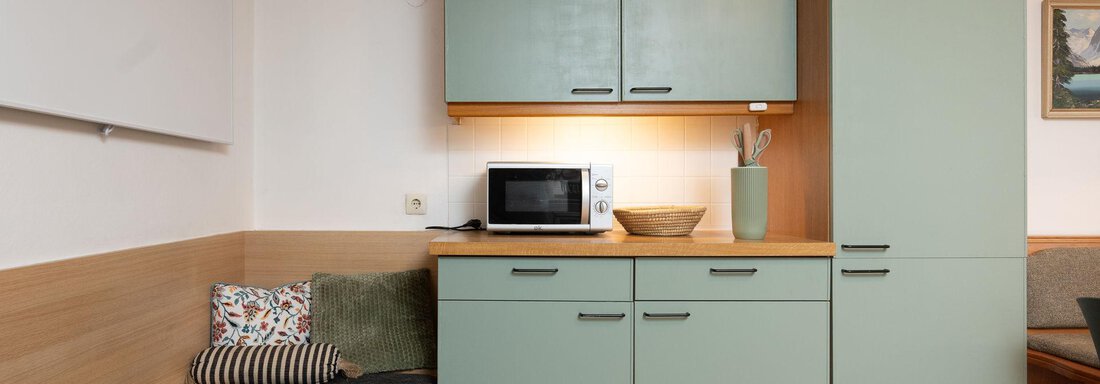 A modern kitchen with green cabinets and a microwave oven. A cozy seating area is also available. - Ferienhaus Valsora - Sölden