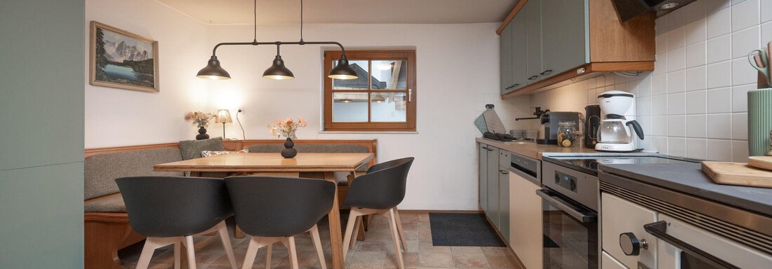 A modern kitchen with a dining area and a large table. The walls are bright, and the furniture is in neutral colors. - Ferienhaus Valsora - Sölden