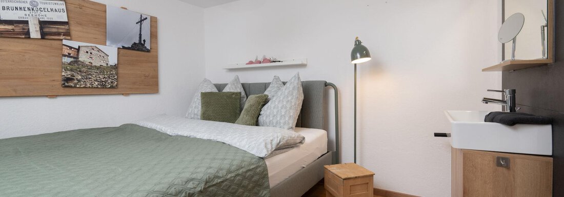 A modern bedroom with a cozy bed and green bedding. The decor is simple and features bright wood tones. - Ferienhaus Valsora - Sölden