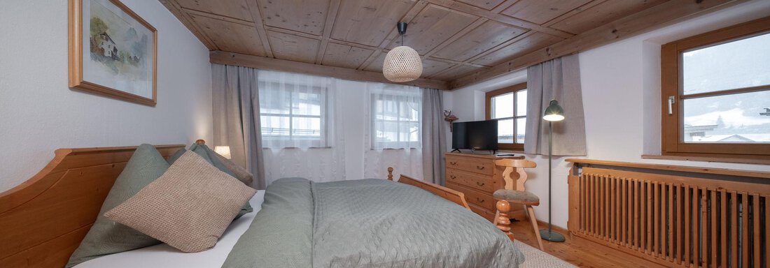 A cozy bedroom with wooden furniture and a large window. The ceiling is made of wood and the room is bright and inviting. - Ferienhaus Valsora - Sölden