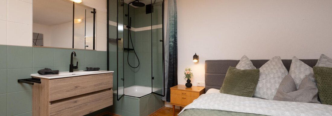 A modern bedroom with a comfortable bed and an adjoining shower. The room is bright and cheerful, featuring a wooden washbasin and decorative cushions. - Ferienhaus Valsora - Sölden