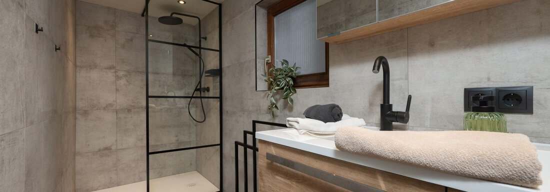 A modern bathroom with a glass enclosure and a comfortable shower. The design combines bright walls with wooden details, creating a cozy atmosphere. - Ferienhaus Valsora - Sölden