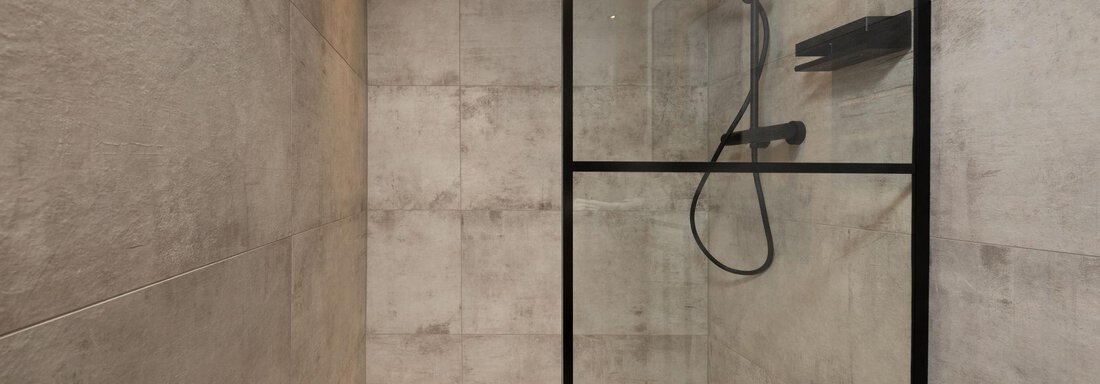 Modern shower with glass door and black fittings. The walls are in neutral shades of gray. - Ferienhaus Valsora - Sölden