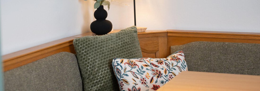 A cozy seating area with gray cushions and a decorative pillow. A table lamp and a vase with dried flowers give the room an inviting atmosphere. - Ferienhaus Valsora - Sölden
