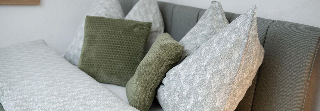 A cozy bedroom with a gray headboard and several pillows in various colors. The duvet is bright and textured, creating an inviting atmosphere. - Ferienhaus Valsora - Sölden