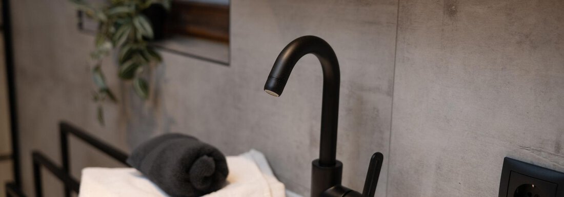 A modern bathroom with a black faucet and fresh towels. In the background, a green plant is visible. - Ferienhaus Valsora - Sölden