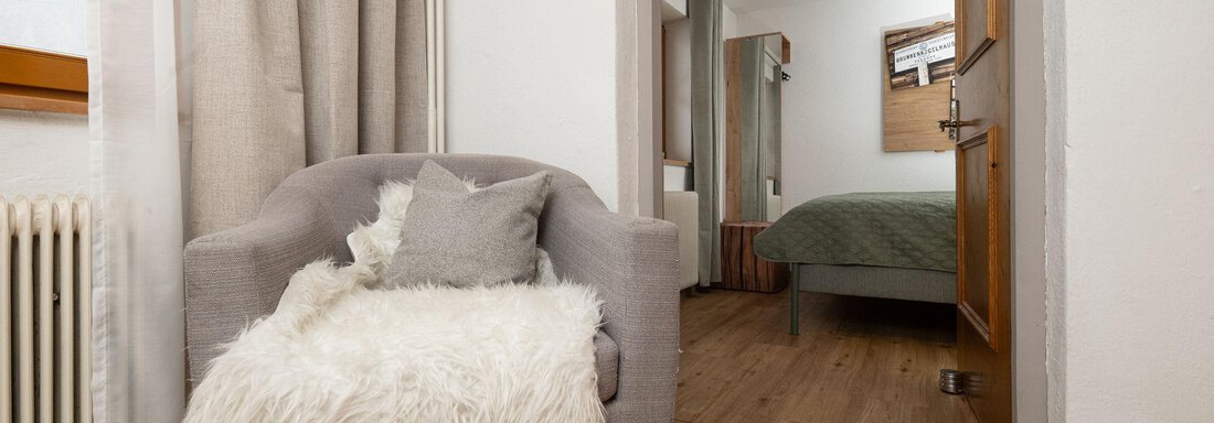 A cozy armchair with a soft cushion is in a bright room. In the background, a bedroom with a bed is visible. - Ferienhaus Valsora - Sölden